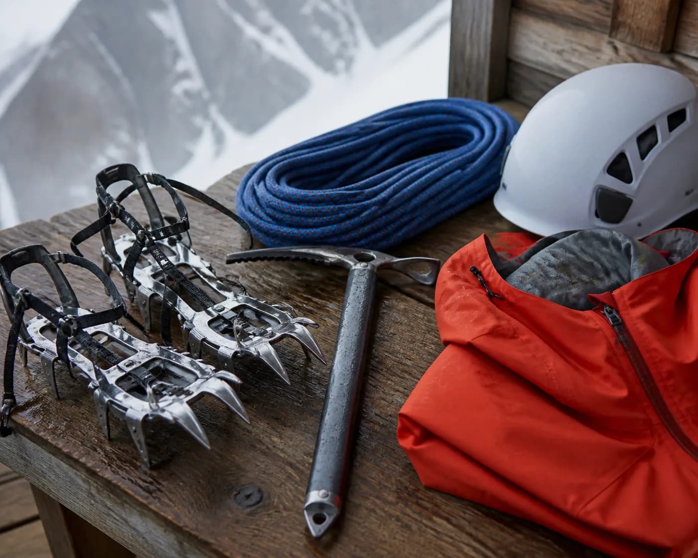 Steigeisen, Eispickel, Seil, Helm und Hardshell-Jacke auf einem Holztisch