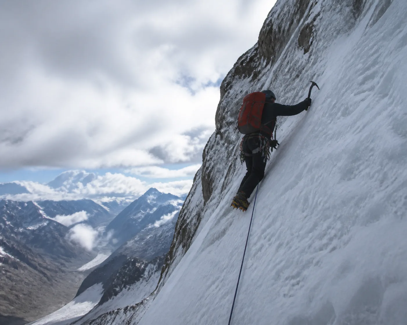 Alpinist im Aufstieg an einer steilen Schnee- und Eisflanke mit Eispickel und Steigeisen